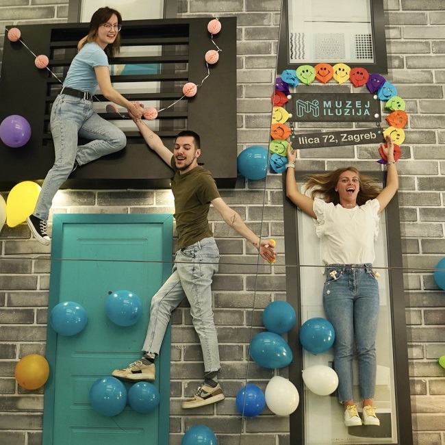 Trois jeunes adultes qui s'amusent dans une salle de musée des illusions de Zagreb.