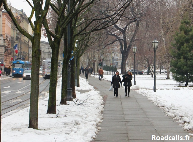 Rue du centre ville de Zagreb en hiver, par temps gris et enneigé, avec des véhicules et quelques piétons.
