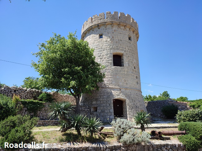 Grande tour en pierre sur les hauteurs de Cres, bordée de palmiers et de murets en pierre.