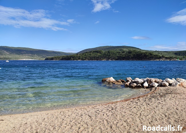 Petite plage de cailloux sur l'île de Cres, avec une mer turquoise et des reliefs verts en arrière plan.