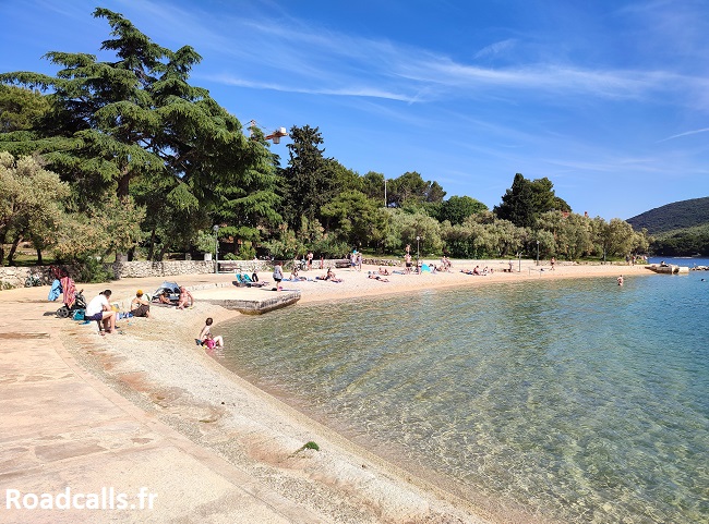 Charmante petite plage de Kimen sur l'île de Cres en Croatie, avec des familles qui bronzent au soleil et au bord de l'eau translucide.