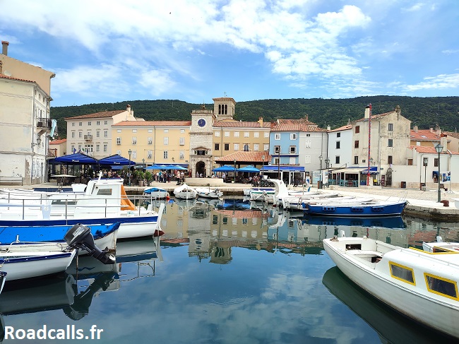 Vue sur le port de Cres avec ses bateaux blancs et ses maisons pastels, avec en arrière-plan les collines vertes.