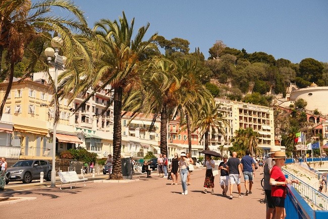 Promenade des Anglais à Nice avec les palmiers et des promeneurs sous le ciel bleu.